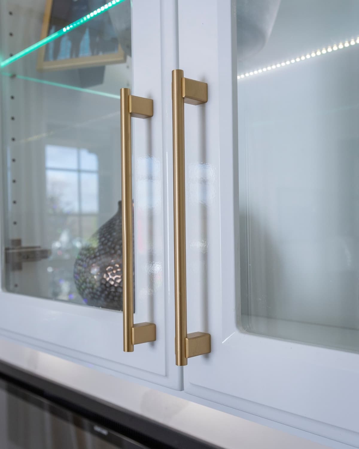 White glass display cabinet with brass handles and LED lighting