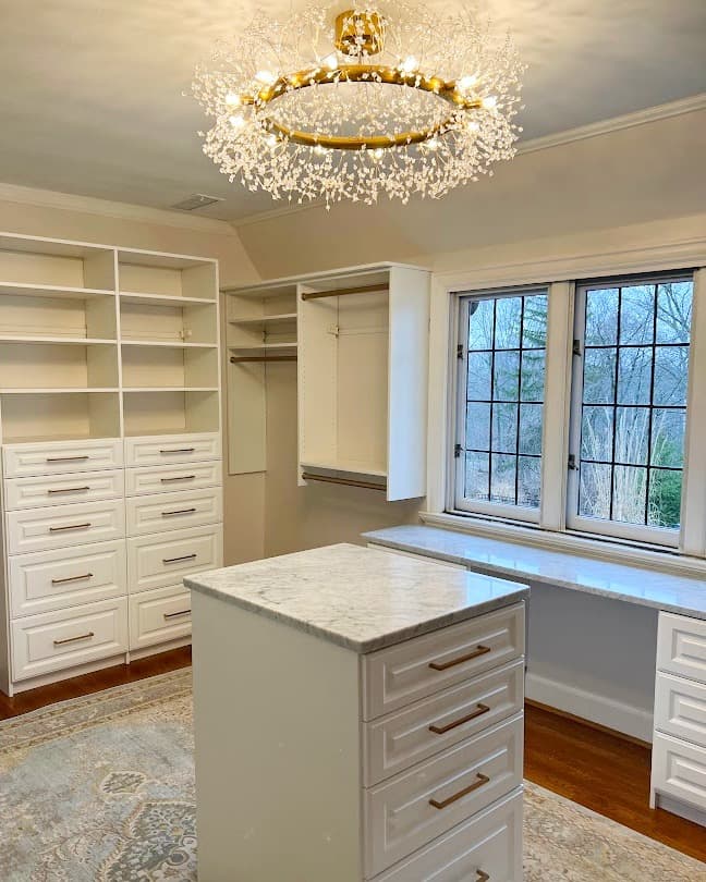 White walk-in closet with gold chandelier and marble island